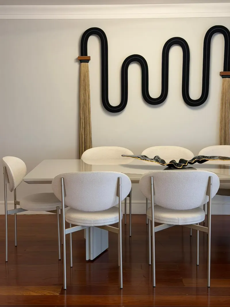 Mesa de jantar branca com cadeiras estofadas e escultura preta na parede
