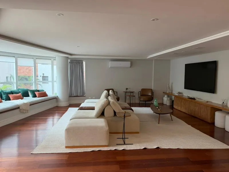 Sala de estar ampla com sofá claro, piso de madeira e janelas em toda a parede