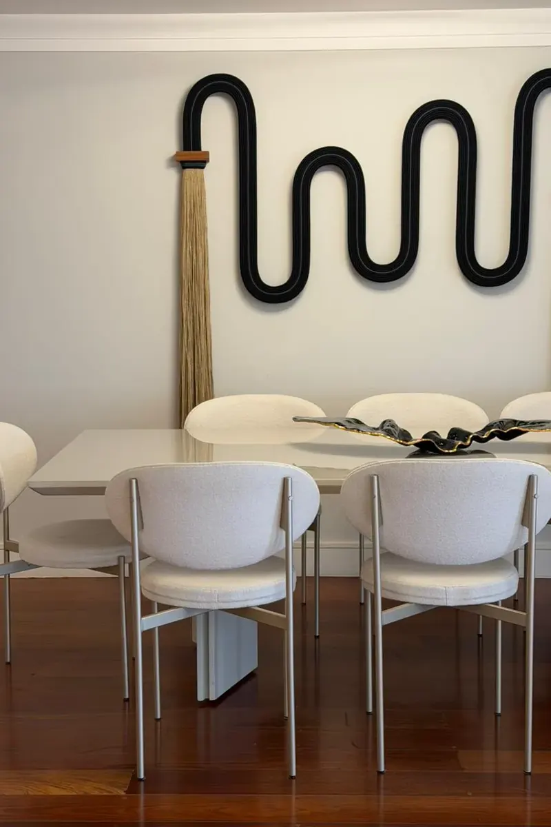 Sala de jantar com mesa branca, cadeiras estofadas e escultura preta na parede