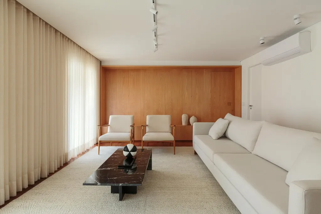 Sala de estar de apartamento de 250 m² com painel em madeira, sofá claro e duas poltronas