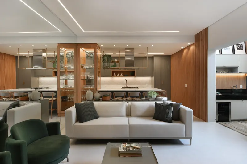 Living com poltronas verdes, escada de pedra e cozinha integrada
